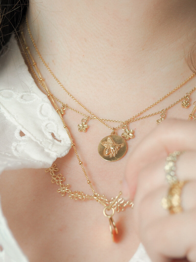 gold flower and bee necklaces layered on model