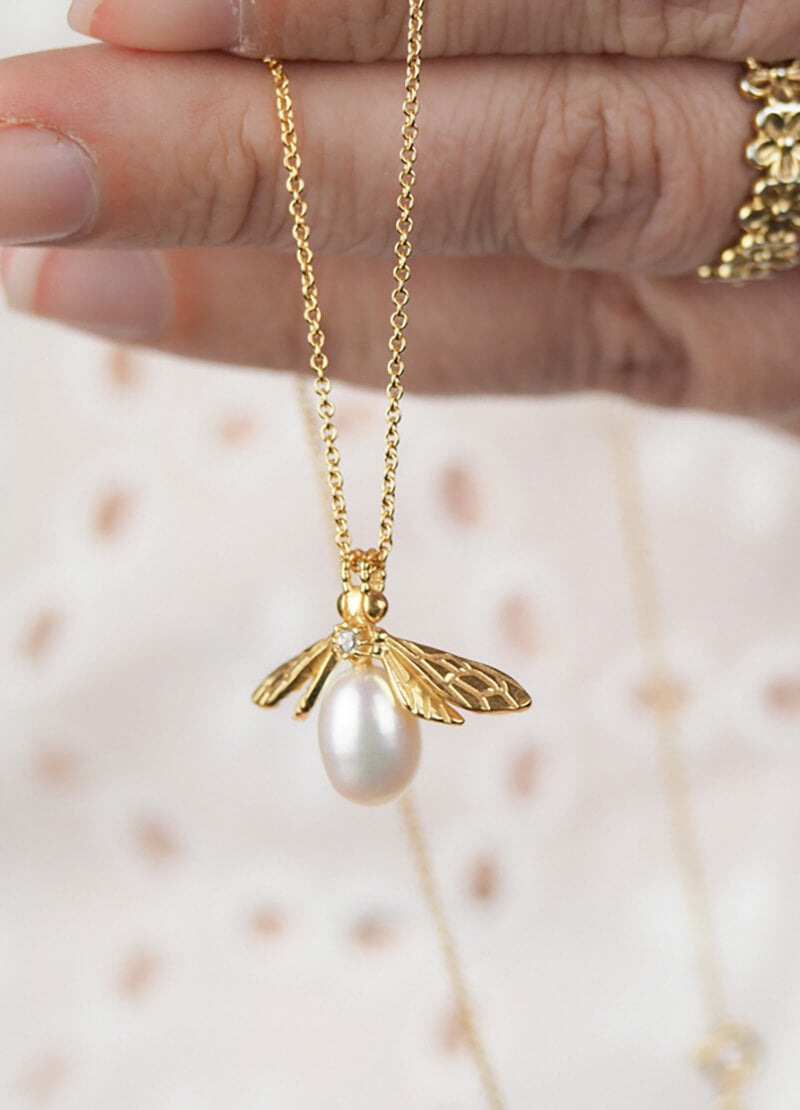 yellow gold pearl bee necklace against lace background