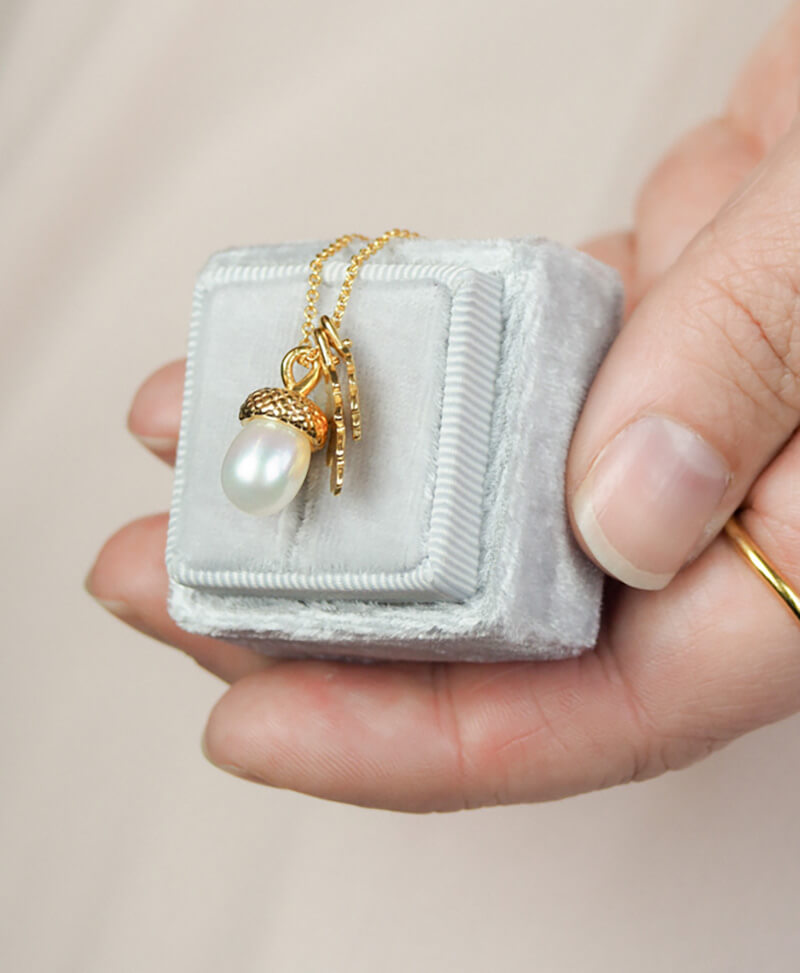 yellow gold pearl acorn necklace with tiny oak leaves on a jewellery box