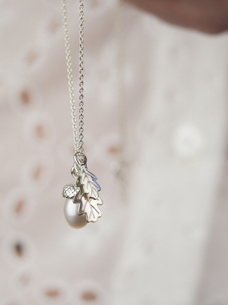 side view of a silver pearl acorn necklace with small oak leaves